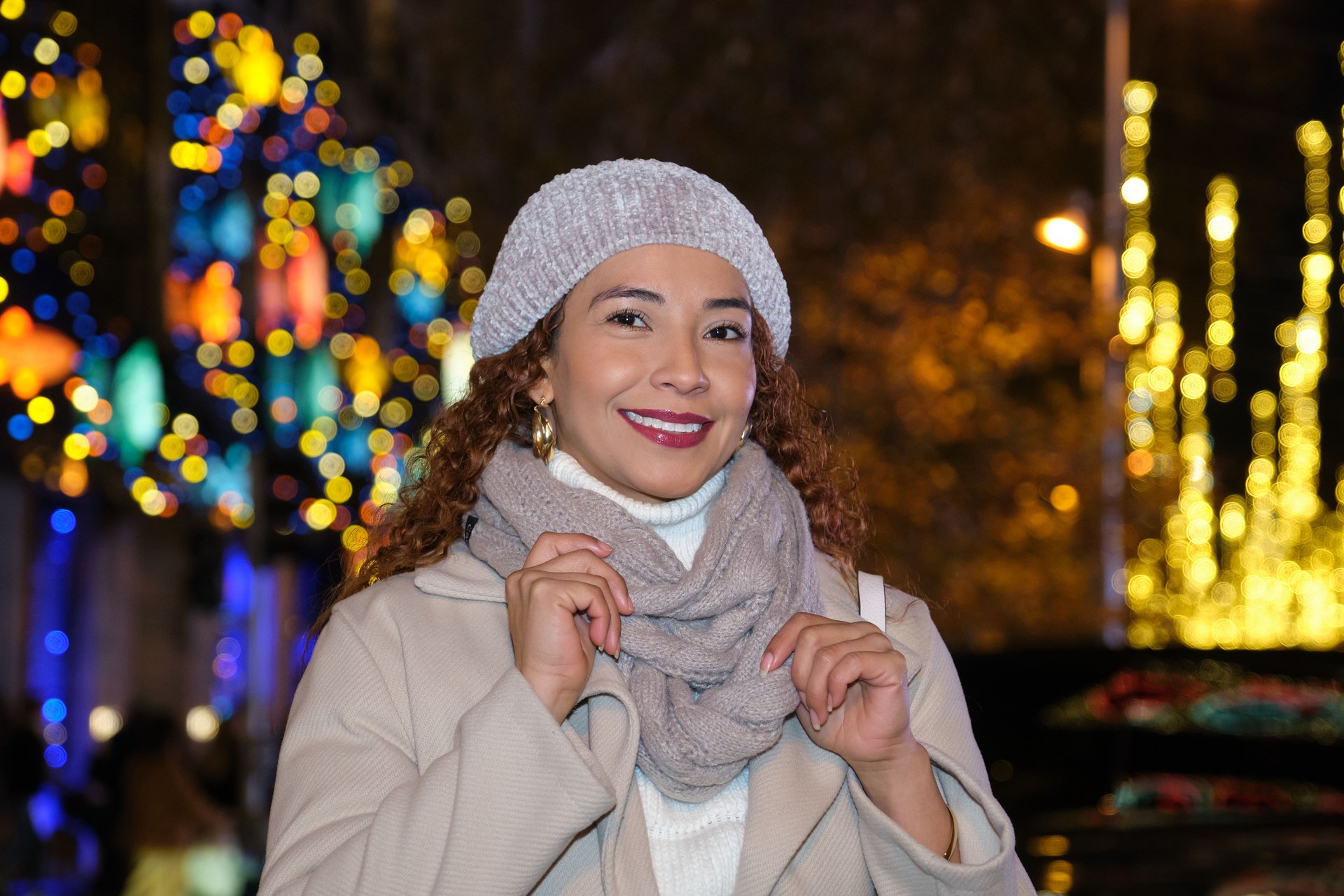 Woman smiling in front of Christmas lights decorations at night